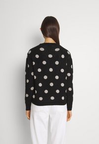Svart ulltröja med stora silverfärgade prickar, ribbade ärmslut och nederkant, med en något avslappnad passform och texturerad stickad struktur.