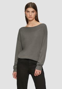 Grijze off-shoulder trui met lange mouwen, geribbelde halslijn en manchetten, gecombineerd met zwarte broek met een soepele textuur.