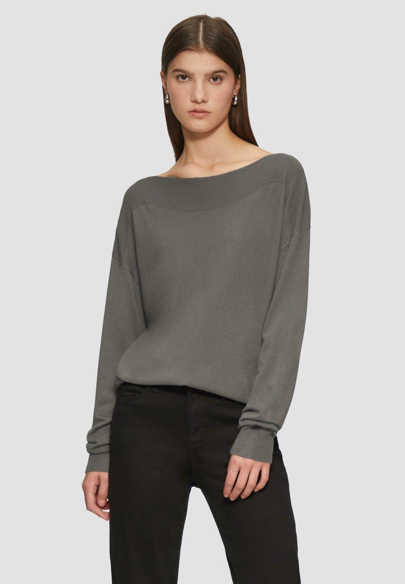 Grijze off-shoulder trui met lange mouwen, geribbelde halslijn en manchetten, gecombineerd met zwarte broek met een soepele textuur.