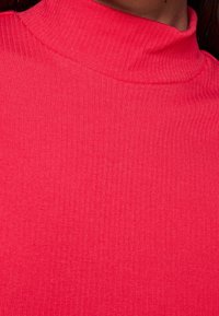 Fittet turtleneck top i lys pink ribbet stof, med høj krave og glat tekstur, som fremhæver en tætsiddende silhuet.