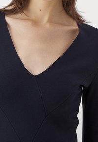 Haut côtelé marine avec un design en V, silhouette ajustée et des détails de couture subtils sur la poitrine et les épaules.