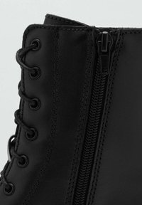 Botín de piel negra hasta el tobillo con una textura suave, ojales de metal redondos, cordones y una cremallera lateral para un fácil acceso.