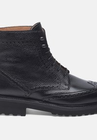 Stivaletto in pelle nera con finitura testurizzata, caratterizzato da dettagli brogue, occhielli in metallo e suola in gomma robusta.
