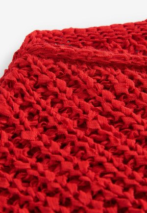 Tessuto rosso lavorato a maglia con un design aperto e testurizzato. Il materiale sembra leggero e flessibile, con anelli e motivi distribuiti su tutta la superficie.