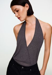 Top gri cu bretele halter și decolteu adânc în V, cu dungi verticale și accente metalice. Purtați cu pantaloni negri cu talie înaltă. Textură netedă.