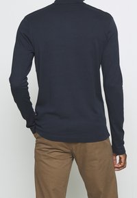 Marinblå långärmad polo med krage, med en slät bomullstextur och en figursydd design, matchad med beige byxor.