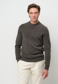 Brun ulltröja med rund halsringning, ribbade ärmslut och nederkant. Buren över krämfärgade byxor som har en mjuk textur och en figurnära design.