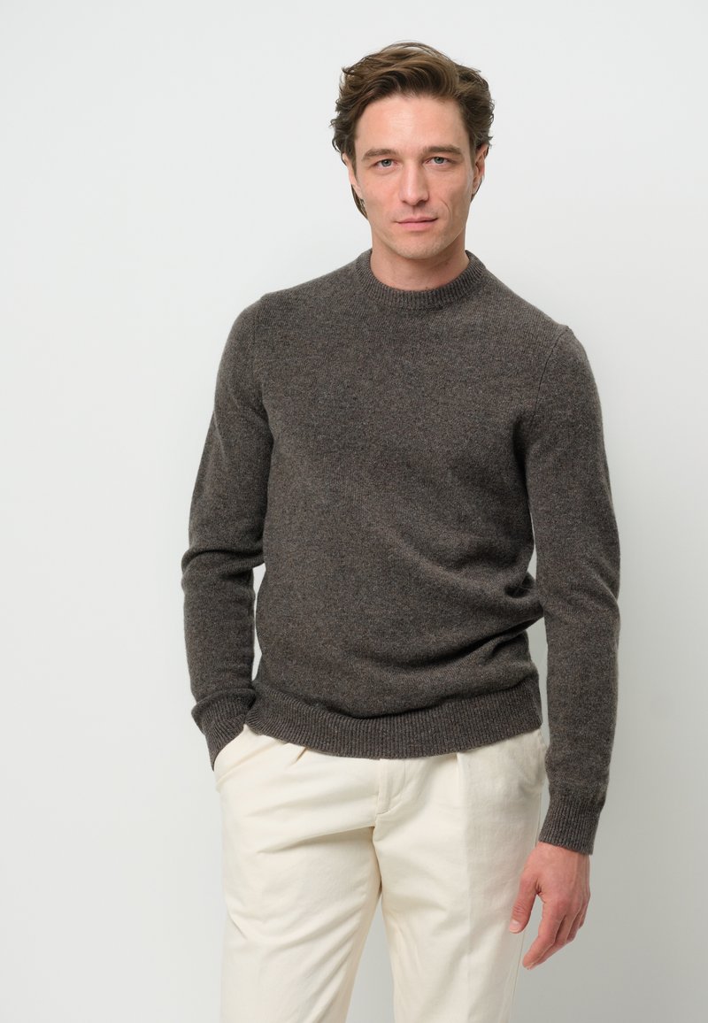 Brun ulltröja med rund halsringning, ribbade ärmslut och nederkant. Buren över krämfärgade byxor som har en mjuk textur och en figurnära design.