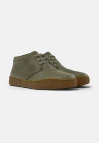Scarpe in pelle verde oliva con design a basso profilo, punte rotonde e chiusura con lacci. Suola in gomma marrone testurizzata con dettaglio di cucitura a contrasto.