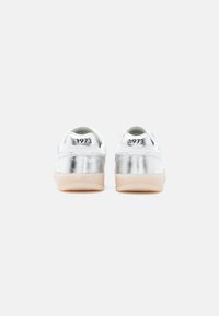 Sneakers metallizzati argento con dettagli bianchi, design basso e suole di gomma beige. Numero modello "1973" sul tallone.