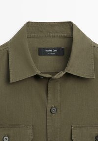 Camicia verde oliva con colletto, chiusura con bottoni, due tasche frontali con patta e etichetta "Massimo Dutti Made in Morocco" all'interno del colletto.