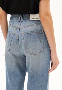 Pantalones de mezclilla azul claro con un corte relajado, que presentan dos bolsillos traseros, una etiqueta de marca en la cinturilla y detalles de costura visibles.
