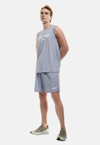 Lys grå atletisk sæt bestående af en ærmeløs top og shorts, begge med "KEEP READY" tekst. Mesh tekstur og afslappet pasform, parret med beige sneakers.