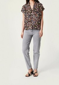 Zwarte bloemetjesblouse met korte mouwen, met multicolore bloemenpatronen. Gemaakt met lichtgrijze jeans en zwarte hoge sandalen.