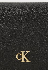 Juodas tekstūruotas piniginė, pagaminta iš odos, su aukso spalvos "CK" logotipu. Kompaktiškas dizainas su lygiu paviršiumi ir subtilia grūdėta tekstūra.