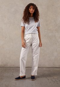 Pantaloni bianchi a vita alta, camicia a righe blu e bianche a maniche corte, espadrillas blu navy, sfondo testurizzato.