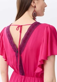 Rosa Kleid mit tiefem V-Rücken, ausgestattet mit einem strukturierten lila Spitzenbesatz, zarter Kordelverschluss und herabfallenden Rüschensäumen.