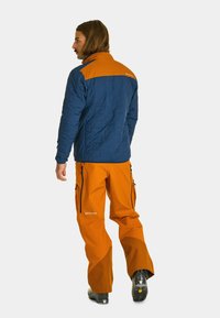 Navy blue quilted jacket with orange shoulders, paired with bright orange pants featuring zippers and black accents.