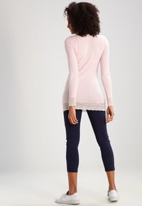 Vaaleanpunainen pitkähihainen paita, jossa on pitsireunus helmassa, yhdistettyinä tummansiinisiin legginsseihin ja valkoisiin lenkkareihin. Siisti pinta, jossa on kampausyksityiskohtia.