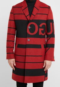 Czerwono-czarny płaszcz z mieszanki wełny z wyrazistym paskowanym wzorem, z klapami ze wcięciem i dwoma przednimi guzikami, o dopasowanym kroju.