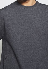 Sudadera de cuello redondo en gris oscuro, confeccionada con tela suave. Presenta un cuello acanalado y detalles en las costuras laterales, con un ajuste relajado.