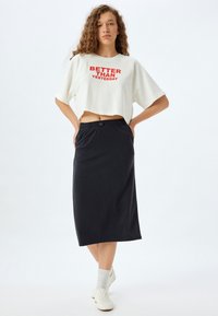 Hvid cropped t-shirt med rød print med teksten "BEDRE END I GÅR," parret med sort lang nederdel med elastisk talje. Hvide sneakers og sokker.