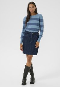 Blauw en marineblauw gestreepte longsleeve trui, gecombineerd met een donkere denim rok met schuine naden en een sluiting met knopen aan de voorkant, en zwarte kniehoge laarzen.