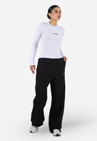 Langermet hvit skjorte med "PEGADOR" logo, kombinert med løse svarte joggebukser. Begge er laget av mykt stoff; buksene har strikket midje.