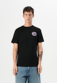 Zwarte katoenen t-shirt met een ronde hals en korte mouwen. Kenmerkt zich door een meerkleurige grafische patch op de linkerborst. Casual pasvorm.