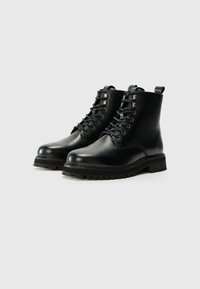 Botas de tobillo de cuero negro con punta redonda, con cordones en la parte frontal, suela de goma resistente y tira en la parte trasera, con un acabado suave.