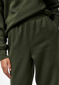 Grüner Pullover und Hose aus weichem Baumwollmischgewebe. Mit elastischem Bund und lässiger Passform. Subtile Textur ohne Muster.