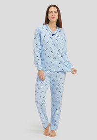 Conjunto de pijama azul claro con camiseta de manga larga y pantalones, que presenta un patrón floral, escote en V y detalles de bolsillo; tejido suave, corte relajado.