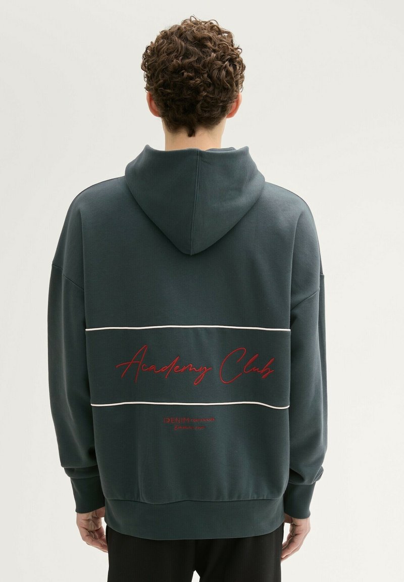 Ciemnozielona bluza z kapturem z przednią kieszenią typu kangur, białymi poziomymi paskami oraz napisem "Academy Club" na plecach w kolorze czerwonym. Miękka tekstura materiału.