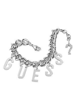Bracelet chaîne en argent avec de grandes breloques lettres formant "GUESS" et une petite breloque en forme de point d’interrogation ornée de strass près du fermoir.