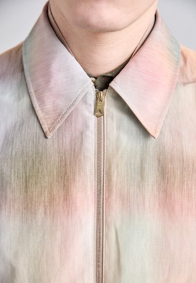 Giacca leggera e texturizzata con un motivo a gradiente in tonalità di rosa chiaro e beige. Presenta una chiusura con zip e un colletto a punta.