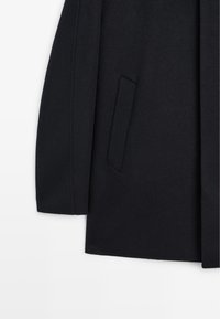 Cappotto di lana su misura in un elegante blu navy con una texture morbida e liscia. Presenta ampie tasche laterali e spalle ben strutturate.