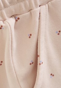 Rosa tyg med en mjuk textur, prytt med små bruna, blå och lila prickar. Visar en midjeresår och en söm för framfickan.