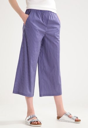 Purple striped wide-leg pants with an elastic waistband and side pockets, paired with silver sandals featuring a buckled strap.