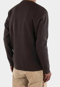 Brun långärmad crewneck-tröja med texturerad tyg. Har en avslappnad passform och minimal sömnad. Matchas med ljusbeige byxor.