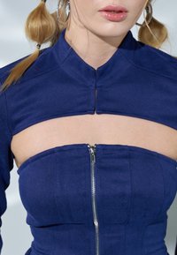 Blue structured top with a high collar and cutout design. Features a front zipper and textured fabric with subtle patterns.