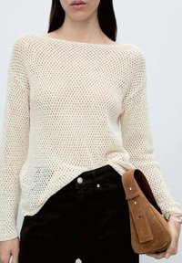 Pull en tricot crème clair à maille ouverte, encolure large et manches longues. Associé à un jean foncé et un sac à main en daim marron.