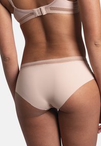 Sous-vêtements beige sans coutures avec une texture lisse, présentant une délicate bordure en dentelle le long de la taille, conçus pour le confort et l'ajustement.