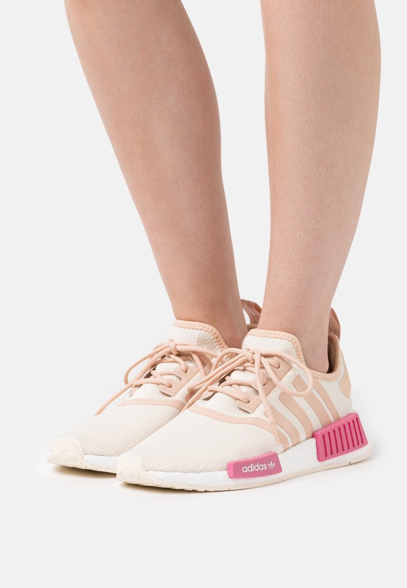 Ljusrosa Adidas-sneakers med stickad ovandel, gummisula och djärv rosa accent på hälen. Snörningsdesign med tre ränder på sidan.