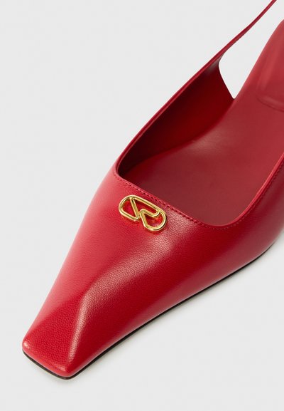 Chaussure rouge en cuir à bout pointu avec une coupe basse, ornée d'un accent en or près de l'ouverture et d'une texture lisse sur la surface.