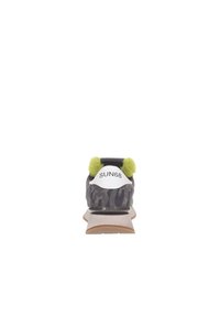 Zapatilla con una parte superior de camuflaje gris, pompones verdes brillantes en el talón y un logo blanco. Suela marrón clara y detalles mínimos.
