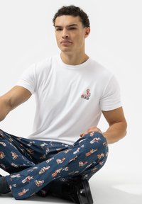 Witte katoenen t-shirt met een kleine kleurrijke grafiek op de borst, gecombineerd met blauwe pyjamabroek met verschillende speelse ontwerpen.