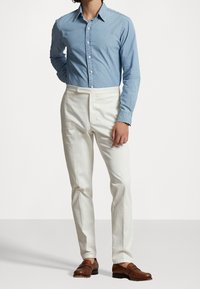 Ljusblå denimskjorta med knappar, i kombination med vita skräddarsydda byxor och bruna läderloafers. Enkelt design och strukturerad form.