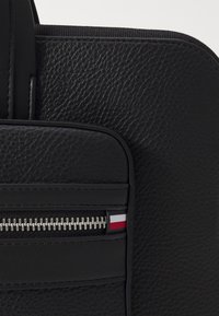 Black leather bag features a textured finish, vertical zippered pocket, and a small accent stripe in red, white, and blue.