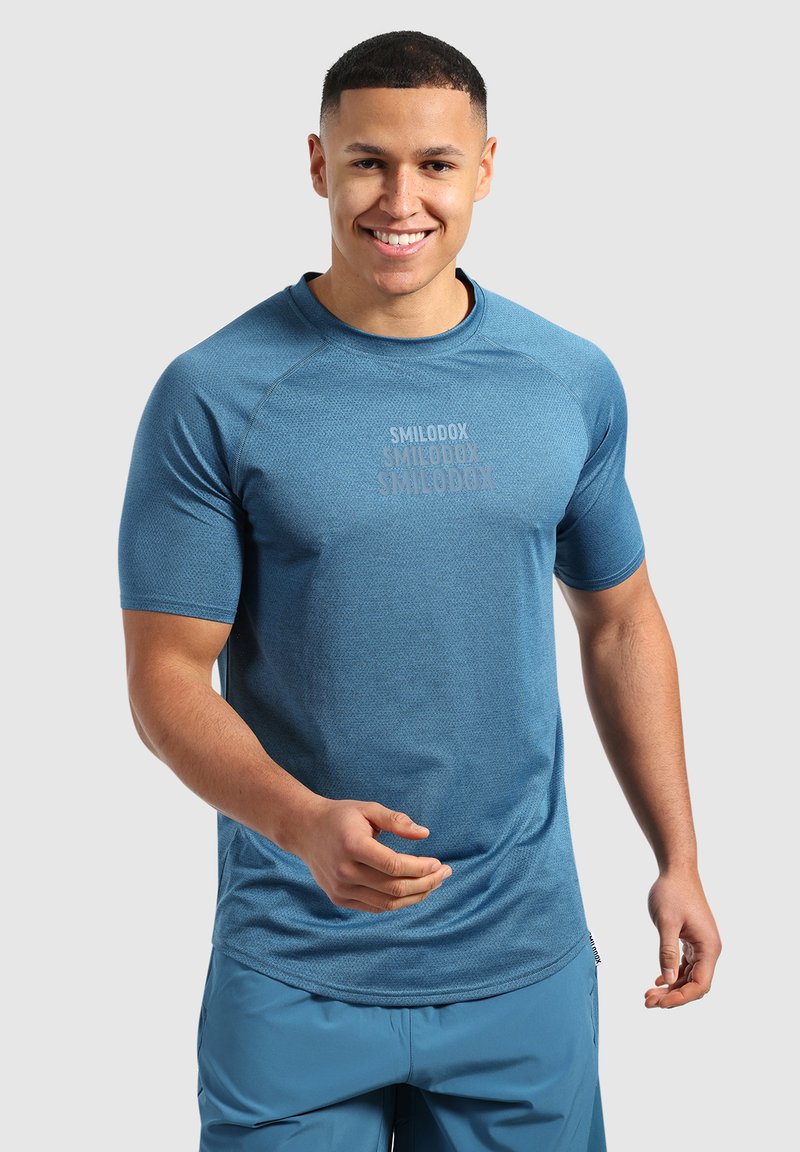 Niebieska koszulka sportowa z krótkim rękawem, okrągłym dekoltem i strukturalną tkaniną. Posiada logo nadrukowane w okolicy klatki piersiowej.