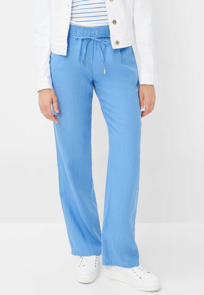 Pantalons bleu clair, amples, avec une taille élastique et un cordon de serrage, associés à des baskets blanches. Tissu lisse et respirant.